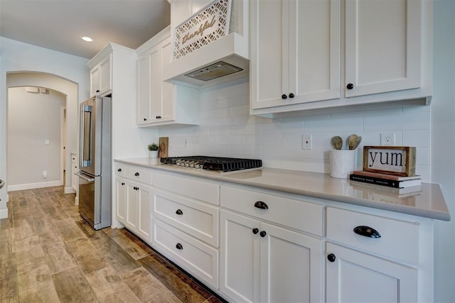 kitchen featuring stainless steel appliances, tasteful backsplash, white cabinets, custom exhaust hood, and light wood-type flooring