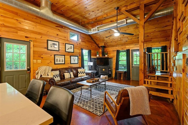 living room featuring a wood stove, wood walls, plenty of natural light, and high vaulted ceiling