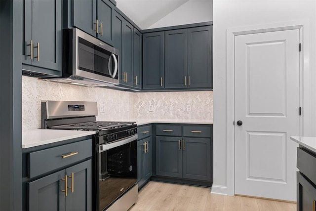 kitchen featuring gray cabinetry, lofted ceiling, decorative backsplash, light wood-type flooring, and stainless steel appliances