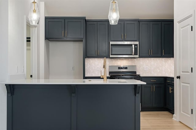 kitchen with decorative light fixtures, backsplash, appliances with stainless steel finishes, and light hardwood / wood-style flooring