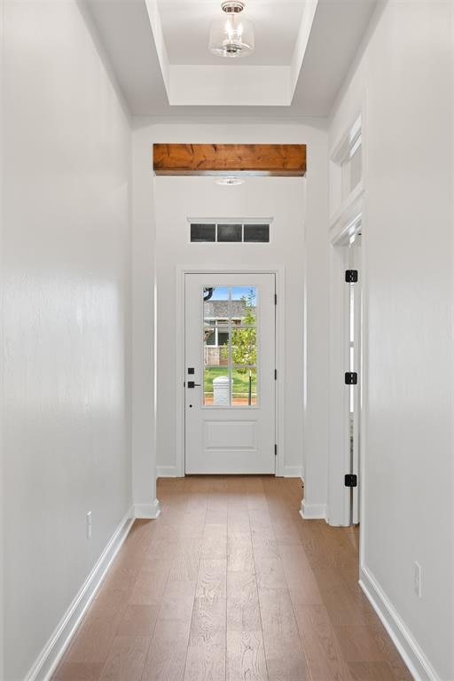 doorway to outside with a tray ceiling and light hardwood / wood-style flooring