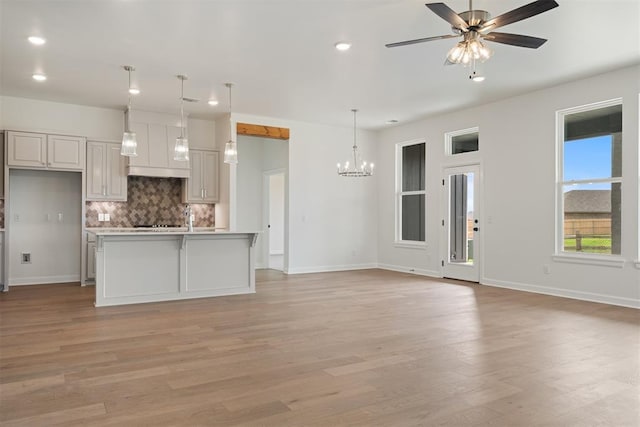 kitchen with a kitchen island with sink, ceiling fan with notable chandelier, hanging light fixtures, light wood-type flooring, and white cabinetry