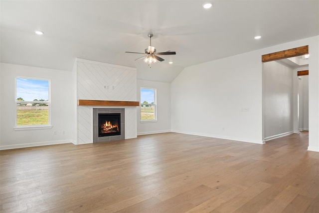 unfurnished living room with a tile fireplace, light wood-type flooring, ceiling fan, and lofted ceiling