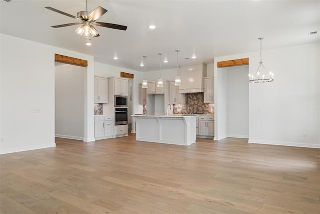 unfurnished living room with sink, ceiling fan with notable chandelier, and light wood-type flooring