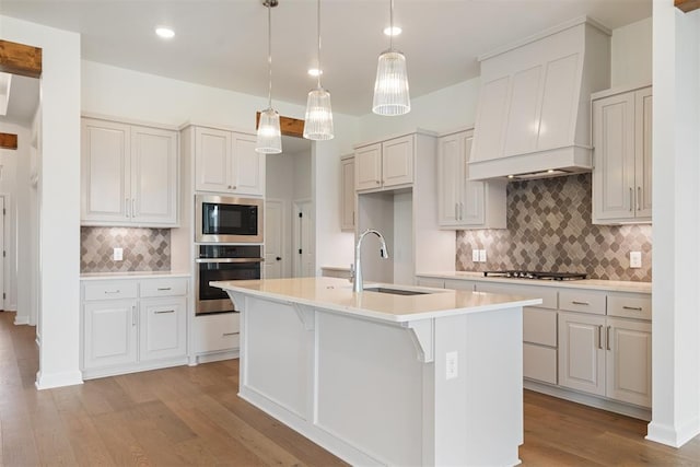 kitchen featuring a kitchen island with sink, sink, light wood-type flooring, white cabinetry, and stainless steel appliances