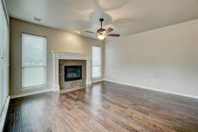 unfurnished living room with ceiling fan, a high end fireplace, and dark wood-type flooring