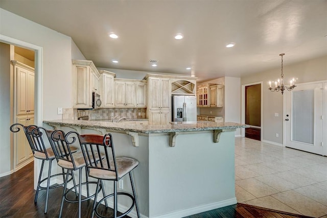 kitchen featuring light stone countertops, hanging light fixtures, stainless steel appliances, a notable chandelier, and a kitchen bar