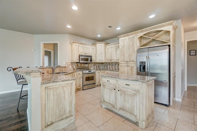 kitchen featuring light stone countertops, kitchen peninsula, a breakfast bar, a kitchen island, and appliances with stainless steel finishes