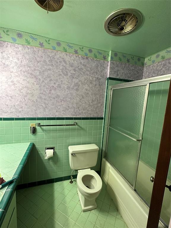 bathroom featuring tile patterned floors, toilet, tile walls, and bath / shower combo with glass door