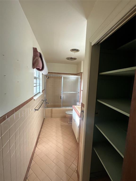 full bathroom with vanity, tile patterned floors, combined bath / shower with glass door, toilet, and tile walls