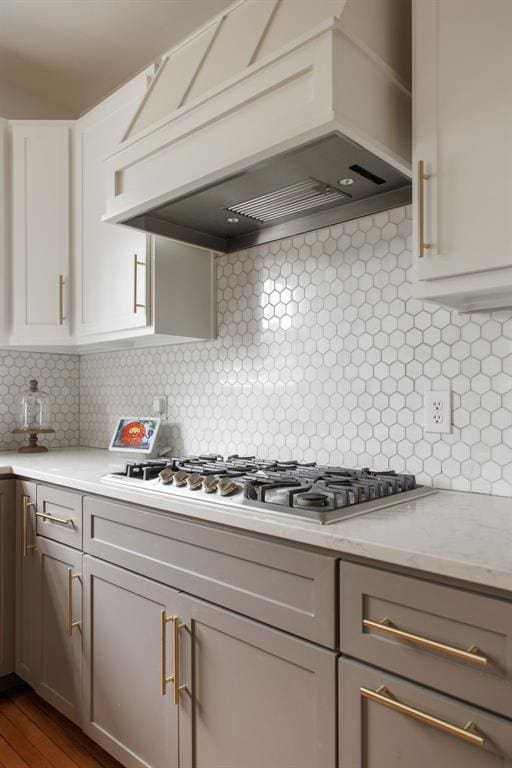 kitchen featuring tasteful backsplash, light stone counters, hardwood / wood-style flooring, and custom exhaust hood