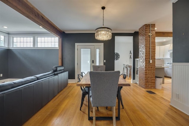 dining room featuring an inviting chandelier, crown molding, light hardwood / wood-style flooring, ornate columns, and beamed ceiling