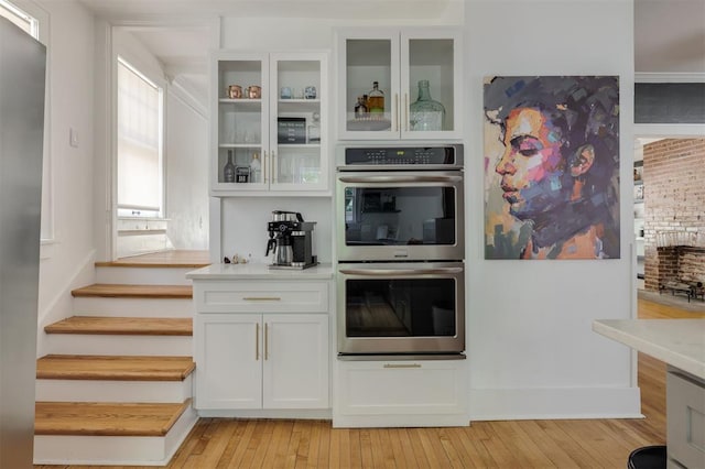 bar with white cabinets, appliances with stainless steel finishes, light hardwood / wood-style floors, and a fireplace