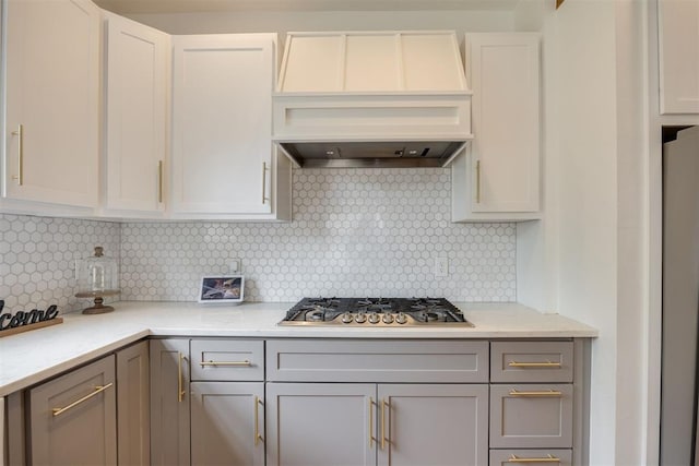 kitchen featuring light stone countertops, stainless steel gas cooktop, white refrigerator, decorative backsplash, and custom exhaust hood