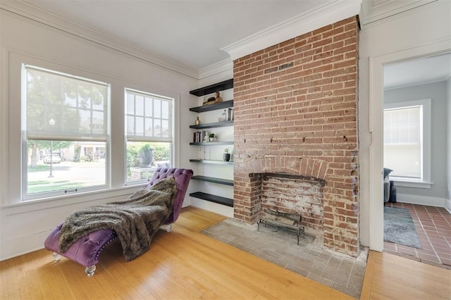 sitting room featuring light wood-type flooring, ornamental molding, and a brick fireplace