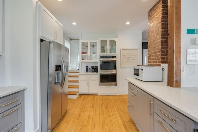 kitchen with gray cabinetry, light stone countertops, stainless steel appliances, white cabinets, and light wood-type flooring