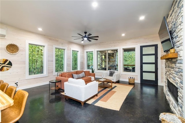 living room with ceiling fan, a stone fireplace, wood walls, and a wealth of natural light