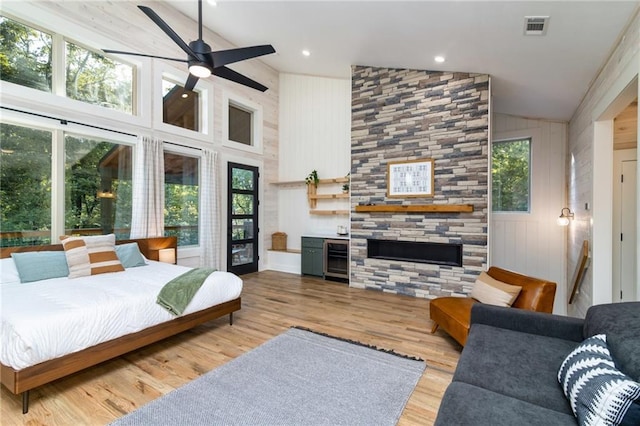 bedroom featuring light hardwood / wood-style flooring, a large fireplace, high vaulted ceiling, and multiple windows