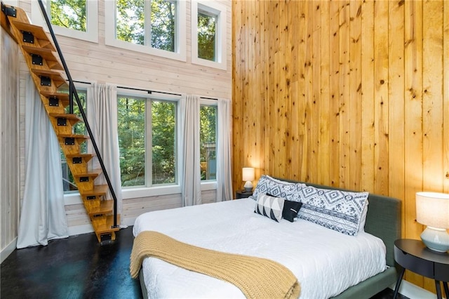 bedroom featuring wooden walls, a high ceiling, and concrete floors