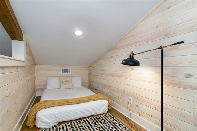 bedroom featuring vaulted ceiling, hardwood / wood-style floors, and wooden walls