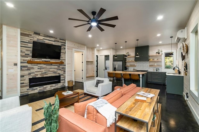 living room featuring ceiling fan, sink, a wall mounted AC, and a stone fireplace