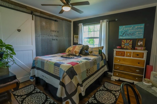 bedroom featuring a barn door, dark hardwood / wood-style floors, ceiling fan, and ornamental molding