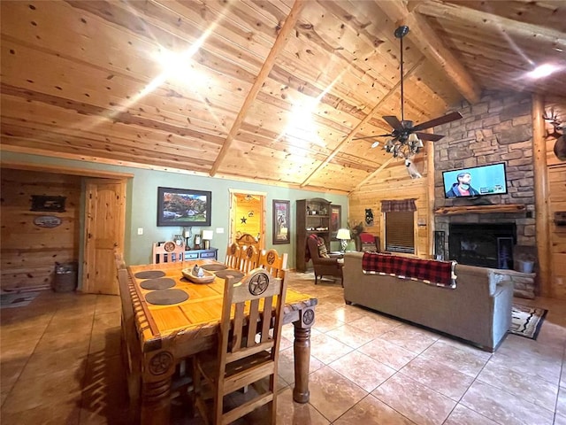 tiled dining room with ceiling fan, wooden ceiling, vaulted ceiling with beams, a stone fireplace, and wood walls