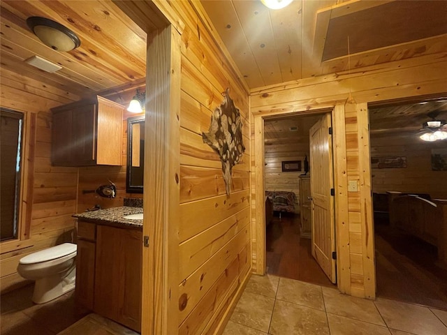 bathroom with tile patterned flooring, vanity, wood walls, and toilet