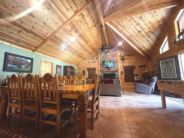 dining space with wooden ceiling, a stone fireplace, tile patterned flooring, beamed ceiling, and wooden walls