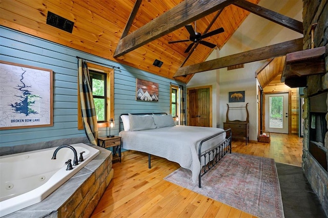 bedroom featuring beamed ceiling, light hardwood / wood-style flooring, multiple windows, and wooden walls