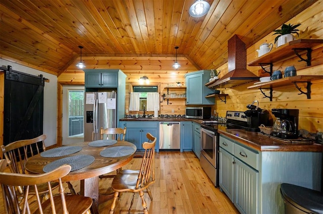 kitchen with wood walls, exhaust hood, vaulted ceiling, a barn door, and appliances with stainless steel finishes