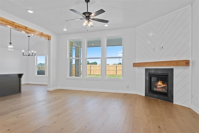 unfurnished living room with a wealth of natural light, a fireplace, ceiling fan with notable chandelier, and light hardwood / wood-style flooring