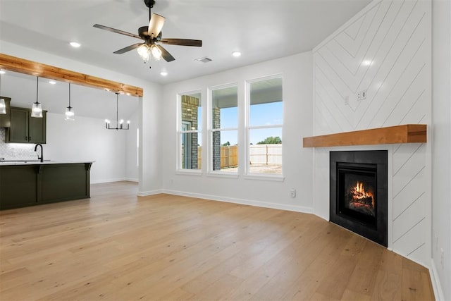 unfurnished living room featuring a fireplace, light hardwood / wood-style floors, ceiling fan, and sink