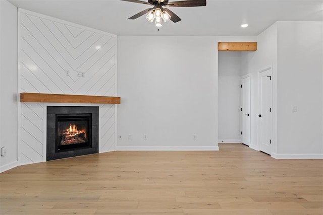 unfurnished living room with ceiling fan, a large fireplace, and light hardwood / wood-style floors