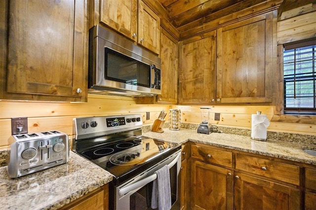 kitchen with appliances with stainless steel finishes, light stone counters, and wood walls