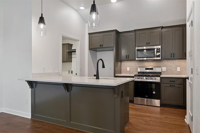 kitchen featuring dark wood-type flooring, kitchen peninsula, decorative light fixtures, a kitchen bar, and appliances with stainless steel finishes