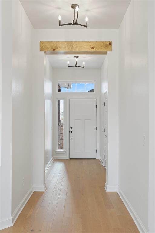 entryway with beam ceiling, an inviting chandelier, and light wood-type flooring