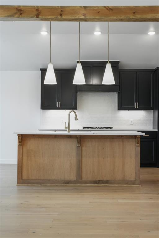 kitchen featuring an island with sink, decorative light fixtures, decorative backsplash, custom range hood, and light wood-type flooring