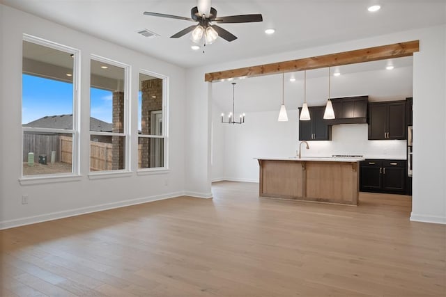 kitchen featuring light wood-type flooring, custom range hood, ceiling fan with notable chandelier, a kitchen island with sink, and pendant lighting