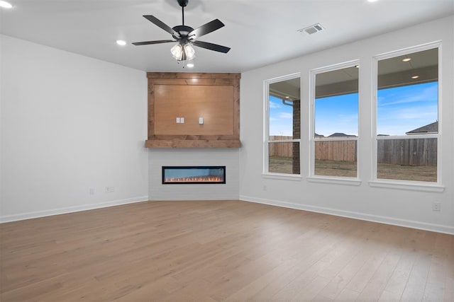 unfurnished living room featuring hardwood / wood-style flooring, ceiling fan, and a fireplace