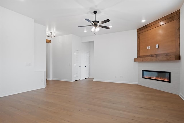 unfurnished living room featuring a large fireplace, light hardwood / wood-style flooring, and ceiling fan