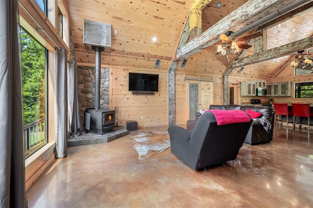 living room featuring ceiling fan, wooden walls, high vaulted ceiling, concrete floors, and a wood stove