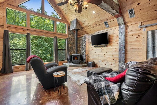 living room with concrete flooring, a wood stove, high vaulted ceiling, and wooden walls