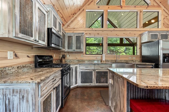 kitchen featuring stainless steel appliances, light stone counters, wood walls, and sink