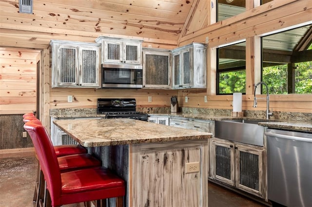 kitchen featuring appliances with stainless steel finishes, a kitchen breakfast bar, vaulted ceiling, a kitchen island, and wood walls