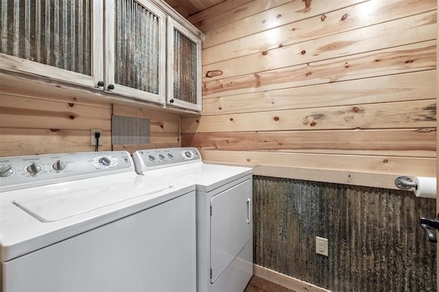 clothes washing area with wooden walls, cabinets, and independent washer and dryer