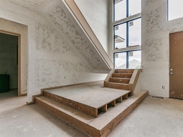 staircase featuring a wealth of natural light, high vaulted ceiling, and concrete flooring