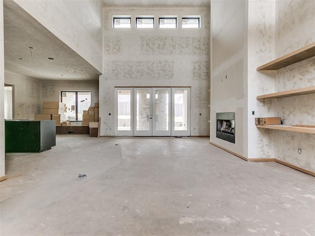 unfurnished living room with concrete flooring, a towering ceiling, and plenty of natural light