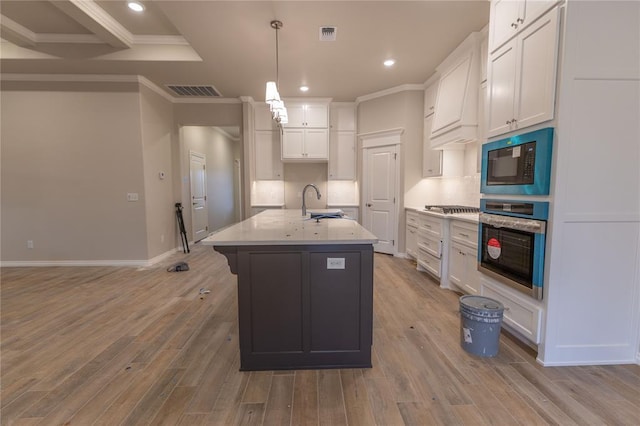 kitchen featuring stainless steel appliances, a kitchen island with sink, pendant lighting, white cabinets, and light hardwood / wood-style floors