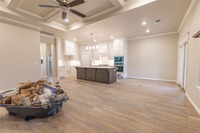 kitchen featuring appliances with stainless steel finishes, light wood-type flooring, a kitchen island with sink, white cabinetry, and hanging light fixtures